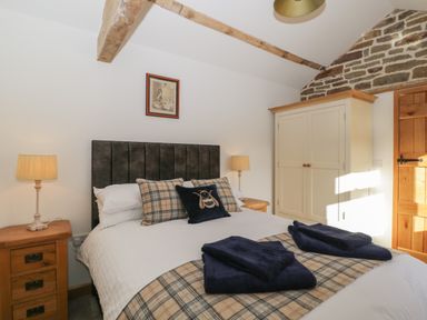 A bedroom with a double bed with plaid pillows and blankets beside wooden nightstands with lamps and a wardrobe against a stone wall at Keepers Barn Bromyard