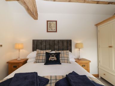 A bedroom with a bed having plaid and bee-themed cushions bedside tables with lamps and a wardrobe at Keepers Barn in Bromyard