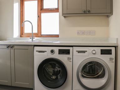 A laundry room with a washer and dryer under a countertop and a sink next to a window at The Cow Shed in Bromyard