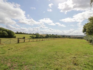 A grassy field with a fence and gate at The Cow Shed in Bromyard