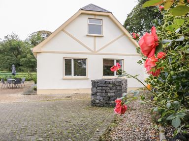 A house with beige walls and three windows with a stone structure and red flowers in front at Shore Road in Culdaff County Donegal