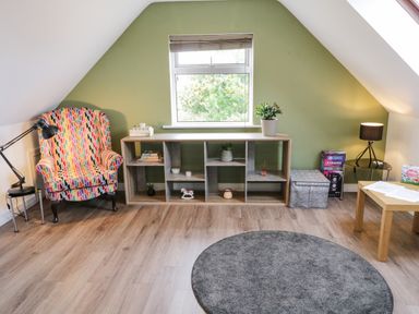 A room with a multicolored armchair a wooden open shelf under a window a gray round rug and a wooden table at Shore Road in Culdaff County Donegal