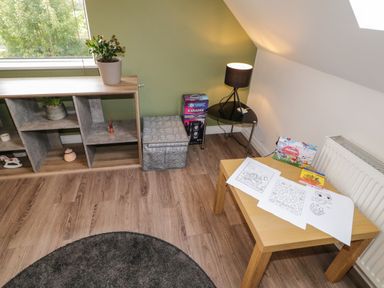 A corner of a room with a wooden table holding coloring pages and crayons a black lamp on a small round table a shelving unit with plants and decor and a window at Shore Road Culdaff County Donegal