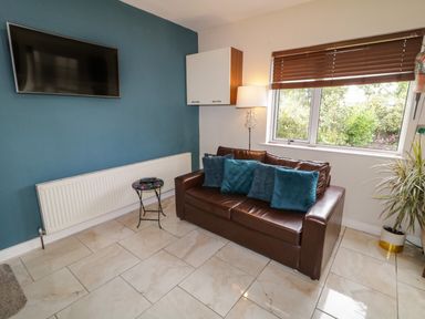 A living room with a brown sofa and blue cushions a small table a wall-mounted television and a window with a blind at Shore Road in Culdaff County Donegal