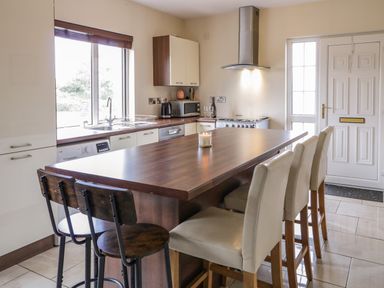 A kitchen with a wooden island counter and chairs a stove and a door at Shore Road Culdaff County Donegal