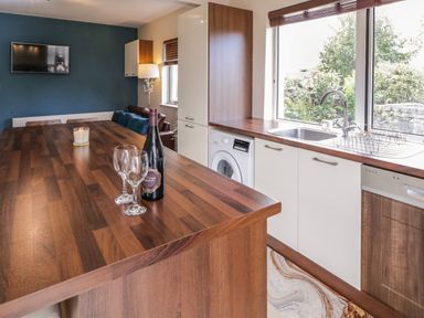 A kitchen with a wooden countertop island with wine bottle and glasses a washing machine under counter and a large window with a view of greenery at Shore Road in Culdaff County Donegal
