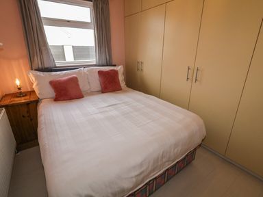 A bedroom with a double bed two red pillows a wooden nightstand with a lamp and large built in wardrobes at Shore Road in Culdaff County Donegal