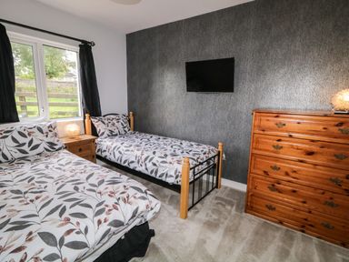 A bedroom with two single beds a wooden dresser a wall-mounted television and a window with black curtains at Shore Road in Culdaff County Donegal