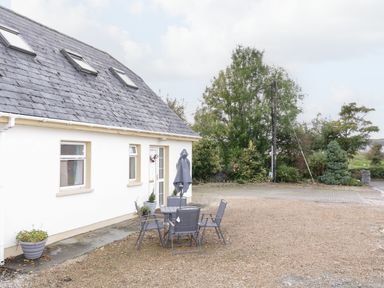 An outdoor patio area with a table and chairs outside a white house with a slate roof and skylights at Shore Road in Culdaff County Donegal