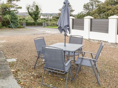 An outdoor patio area with a table four chairs and a closed umbrella on a gravel surface at Shore Road in Culdaff County Donegal