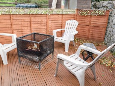 An outdoor patio with four white plastic chairs around a metal fire pit on a wooden deck at Shore Road in Culdaff County Donegal
