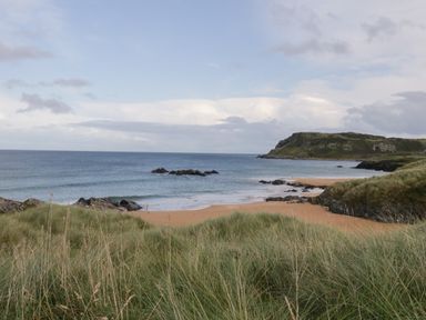 A sandy beach with rocks and grassy dunes overlooking the ocean and a cliff at Shore Road in Culdaff County Donegal