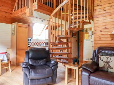 A living room with leather chairs a wooden spiral staircase and a kitchen area at Trout River Retreat Clifford Bridge near Moretonhampstead