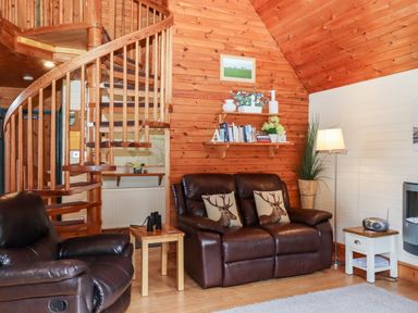 A living room with a wooden spiral staircase leather seating and shelves with books and decorations at Trout River Retreat Clifford Bridge near Moretonhampstead