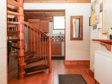 An interior with a wooden spiral staircase hardwood floor kitchen cabinets and a wall-mounted mirror at Trout River Retreat in Clifford Bridge near Moretonhampstead