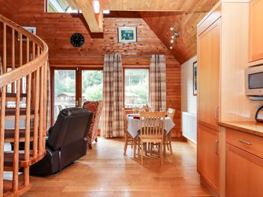 A dining area with a table and chairs beside a window and a spiral staircase in a wooden interior at Trout River Retreat Clifford Bridge near Moretonhampstead