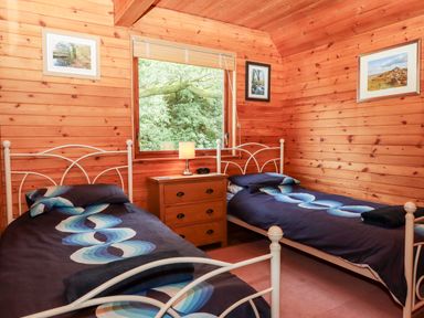 A bedroom with two single beds a wooden dresser and framed pictures on wooden walls at Trout River Retreat Clifford Bridge near Moretonhampstead