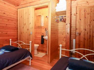 A wooden bedroom with two single beds a small bathroom with toilet and sink and a closet with towels and hangers at Trout River Retreat Clifford Bridge near Moretonhampstead
