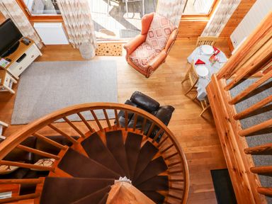 A living area with a spiral staircase a dining table set for two an armchair a TV and a rug at Trout River Retreat in Clifford Bridge near Moretonhampstead