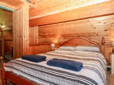 A bedroom with wooden walls a double bed with striped bedding and folded towels at Trout River Retreat Clifford Bridge near Moretonhampstead