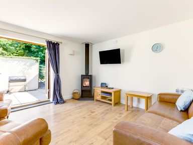 A living room with brown leather sofas a wood stove and TV mounted on the wall at Chy Pol in St Minver
