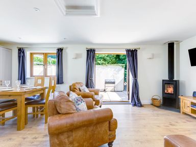 A living room with leather sofas wooden dining table wood stove and open doors to a patio at Chy Pol in St Minver