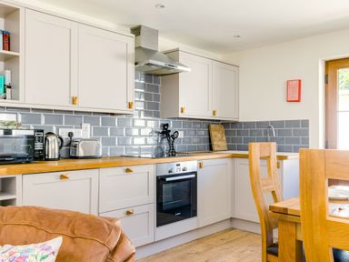 A kitchen with wooden countertops gray tiled backsplash white cabinets and wooden dining chairs at Chy Pol in St Minver