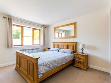 A bedroom with a wooden bed frame a mirror above the bed and two wooden bedside tables at Chy Pol in St Minver