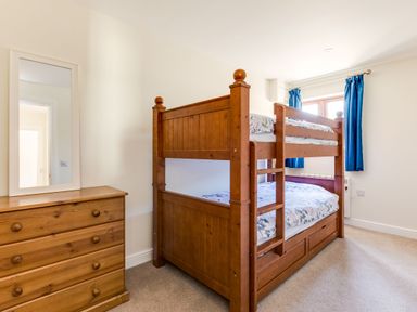 A bedroom with a wooden bunk bed with floral bedding a wooden chest of drawers with a mirror and blue curtains at Chy Pol in St Minver