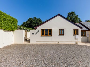 The exterior of a single-story white building with three windows and a gravel driveway at Chy Pol in St Minver