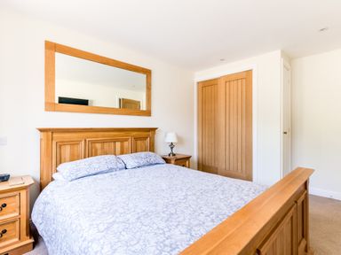 A bedroom with a wooden bed frame a large mirror above the bed wooden bedside tables lamps and a wooden closet door at Chy Pol in St Minver