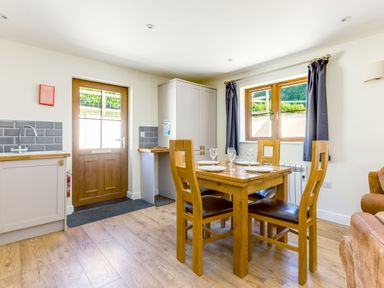 A dining area with a wooden table set with plates and glasses near a window with dark curtains and a wooden door at Chy Pol in St Minver