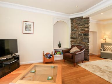 A living room with a leather armchair a wooden coffee table a television and a stone feature wall at Silver How in Ambleside