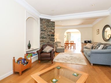 A living room with a glass coffee table a leather armchair a fabric sofa and a dining area visible through an arch at Silver How in Ambleside