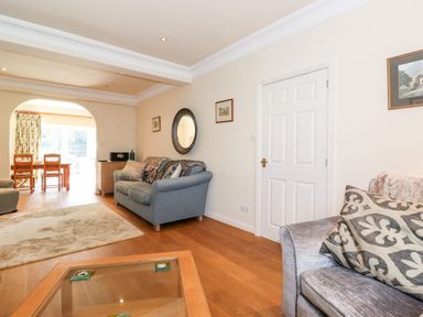 A living room with sofas, a glass coffee table, wall art, and a dining area through an arch at Silver How in Ambleside