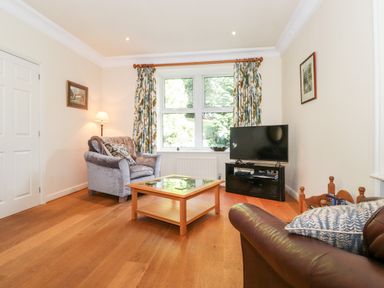 A living room with a gray armchair a wooden coffee table a TV on a stand and floral curtains at Silver How in Ambleside