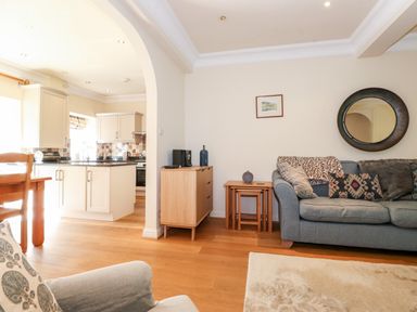 A living room with a grey sofa and wooden nesting tables next to a kitchen with white cabinets and black countertops at Silver How in Ambleside