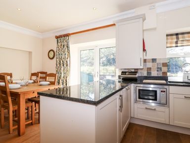 A kitchen with a dining table set with plates and glasses a microwave built into cabinets and French doors with floral curtains at Silver How Ambleside