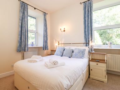 A bedroom with a double bed with towels and blue cushions two windows with blue curtains and two bedside tables at Silver How in Ambleside