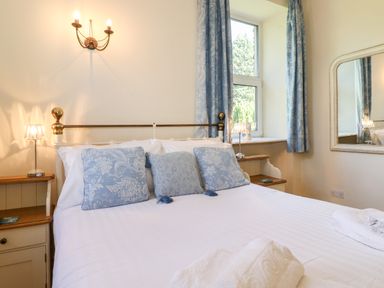 A bedroom with a bed with blue patterned pillows two bedside tables with lamps a window with blue curtains and a wall mirror at Silver How in Ambleside
