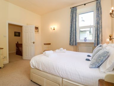 A bedroom with a bed with pillows and towels near a window with curtains and a chair at Silver How in Ambleside