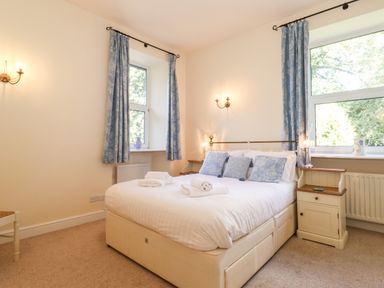 A bedroom with a double bed with blue pillows and white towels near two windows with blue curtains at Silver How in Ambleside