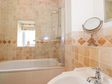 A bathroom with a bathtub shower combination a window a sink and a round tabletop mirror at Silver How in Ambleside