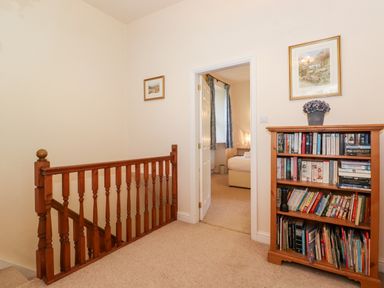 A hallway with a wooden railing, a bookshelf filled with books, and an open door leading to a bedroom at Silver How in Ambleside