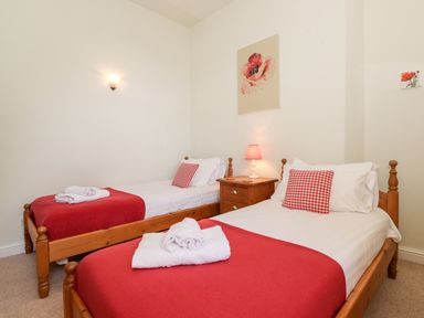 A bedroom with two single wooden beds with red blankets and checkered pillows and a wooden nightstand with a lamp at Silver How in Ambleside