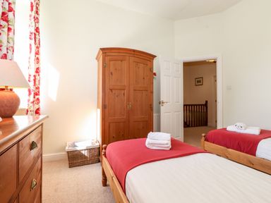 A bedroom with two single beds with red blankets wooden wardrobe chest of drawers and floral curtains at Silver How in Ambleside