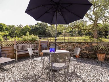 An outdoor seating area with metal chairs and table under a large umbrella and a wooden bench against a wall at Silver How in Ambleside