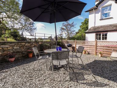 An outdoor patio with a round table and four metal chairs under a large umbrella at Silver How in Ambleside