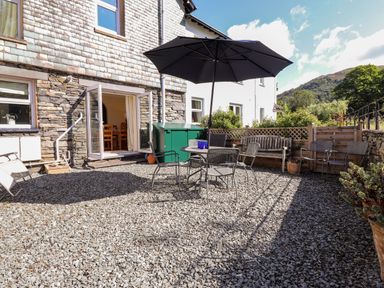 An outdoor patio area with gravel flooring a table with an umbrella and chairs a wooden bench and potted plants at Silver How in Ambleside