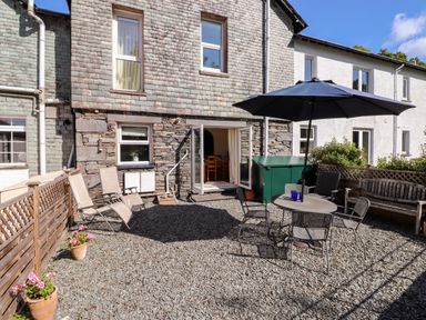 A patio area with outdoor table and chairs under an umbrella two lounge chairs wooden bench and potted plants outside a stone and shingle house at Silver How in Ambleside